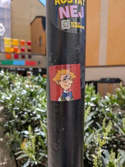 A square red sticker featuring a cartoon character with light skin, curly orange hair, and round glasses. The character has two blue eyes and a distinctive third blue eye on its forehead. It is depicted smiling, wearing a white collared shirt, a blue bow tie, and a green and brown patterned vest. The top left corner contains the text 'ta från de rika.' in white, and the bottom right corner has '@amxkb' in white.