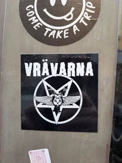 Street sticker A square black sticker featuring the white text 'VRÄVARNA' in a distressed font. Below the text is an inverted pentagram containing a winged, pig-like mascot throwing rock-on hand signs.
