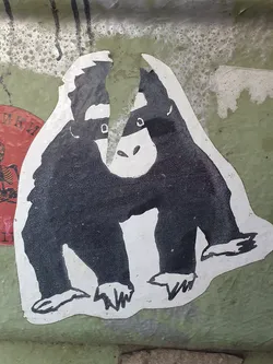 This sticker features a stylized illustration of a monkey wearing a mask, reminiscent of a superhero or secret agent. The design is simple yet striking, with bold black outlines and white background. The sticker appears to be hand-drawn and is slightly damaged around the edges, adding to its unique character.