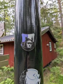 Street sticker A shield-shaped sticker split vertically into purple and white halves. It depicts a shouting figure wearing a black hoodie, cap, and sunglasses in the foreground, with castle spires silhouetted in the background.