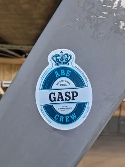 Street sticker An oval-shaped sticker designed to mimic a classic Danish beer label (specifically resembling Tuborg). The sticker is primarily blue and white, topped with a blue crown illustration. The central design features a circular emblem split by a horizontal white banner with the word 'GASP' in bold, dark blue capital letters. Above the banner is the word 'ABE' and below is 'CREW', both in light blue. Various Danish and Swedish texts are printed around the circular frame and edges, including 'HELE DANMARKS PILSNER' and 'BRYGGET SIDEN 1986'.