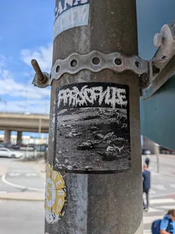 Street sticker A rectangular black and white sticker. The top half features a white, dripping, death-metal style logo reading 'PARASITES'. The bottom half shows a grainy, high-contrast photo of a field strewn with bodies.