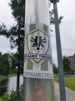 Street sticker A sticker featuring the logo of Dynamo Tresen, a German football club. The logo shows two bears holding mugs above a soccer ball, set against a shield with vertical stripes.  The text "Dynamo Tresen" is clearly visible above the logo, and "fcdynamo.tresen" is printed below.