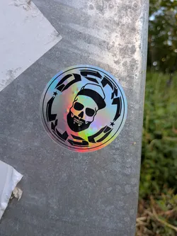 Street sticker A circular holographic sticker with a black print of a bearded skull wearing a cap, enclosed by a circular border containing the stylized word 'DESTROY'.