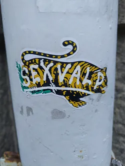 A sticker featuring a tiger with the word SEXVALP written across its body. The tiger is depicted in black and yellow stripes, with green foliage beneath it.