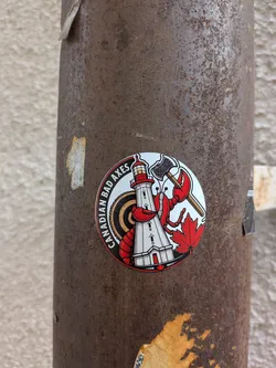 Street sticker A circular sticker on a rusty metal pole. It depicts a red lobster holding a double-bitted axe next to a white lighthouse, with a target background, a red maple leaf, and the text 'CANADIAN BAD AXES' along the left edge.