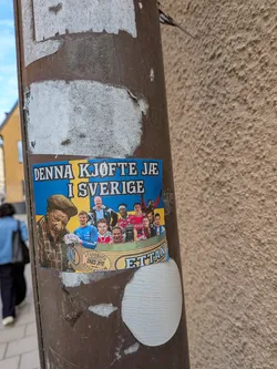 Street sticker The sticker is rectangular with a background mimicking the blue and yellow of the Swedish flag. On the left, an older man with a weathered face, wearing a plaid shirt, suspenders, and a flat cap, holds what appears to be a snus can. To his right, a diverse group of male football players, some in jerseys (red, blue, white), are depicted in a semi-circle, as if in a boat or a celebratory huddle. One player in a blue jersey holds a football. A curved banner at the bottom features text related to snus. The overall style is illustrative and somewhat cartoonish, combining elements of traditional Swedish identity with modern sports.