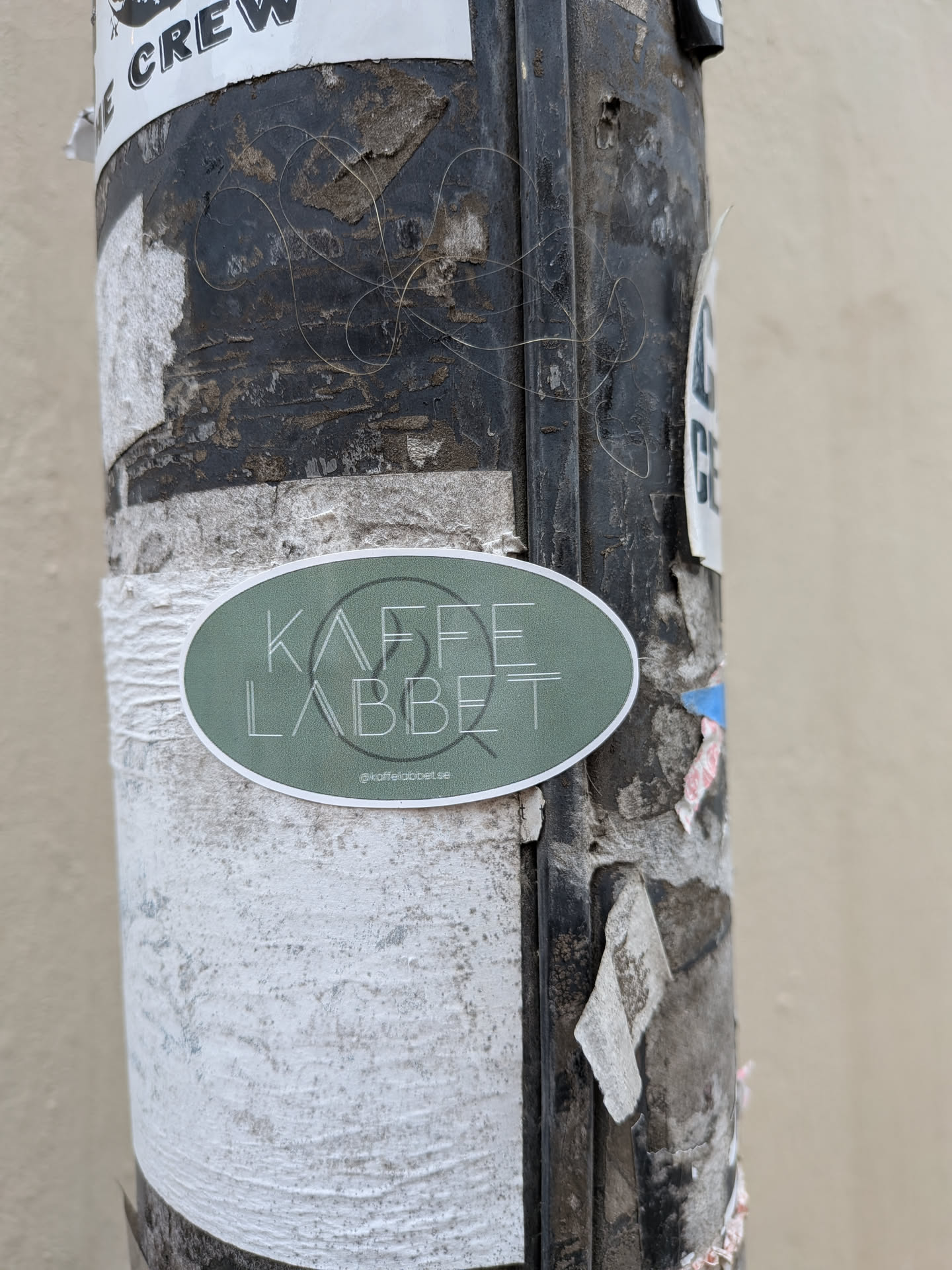 An oval-shaped sticker with a muted sage green background and a thin white border. The sticker features the text 'KAFFE LABBET' in a thin, white, stylized sans-serif font. Behind the text is a faint, thin-line circular logo. At the bottom, there is a small Instagram icon followed by the handle 'kaffelabbet.se'.