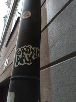 Street sticker A green and white sticker with the words "GRÖNA ARKET" in a stylized font. The sticker is affixed to a dark gray metal pole on the side of a building.