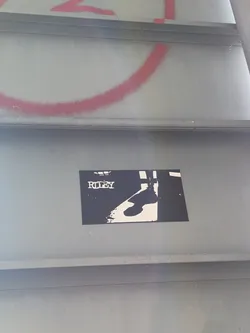 Street sticker The sticker is rectangular and predominantly black with white elements. At the top, the word 'RILEY' is printed in a distressed, stencil-like white font. Below the text, a silhouette of a person's lower legs and feet is depicted in white against the black background. The silhouette appears to be walking or standing, with one leg slightly forward. The overall aesthetic is minimalist and graphic.