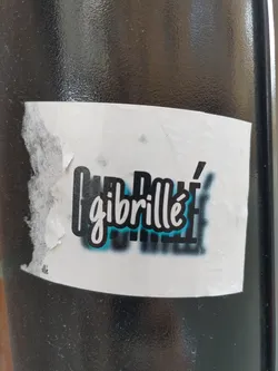 Street sticker A sticker featuring the word "Gibrillé" in stylized lettering with a teal and black color scheme.  The sticker is slightly damaged at one corner.