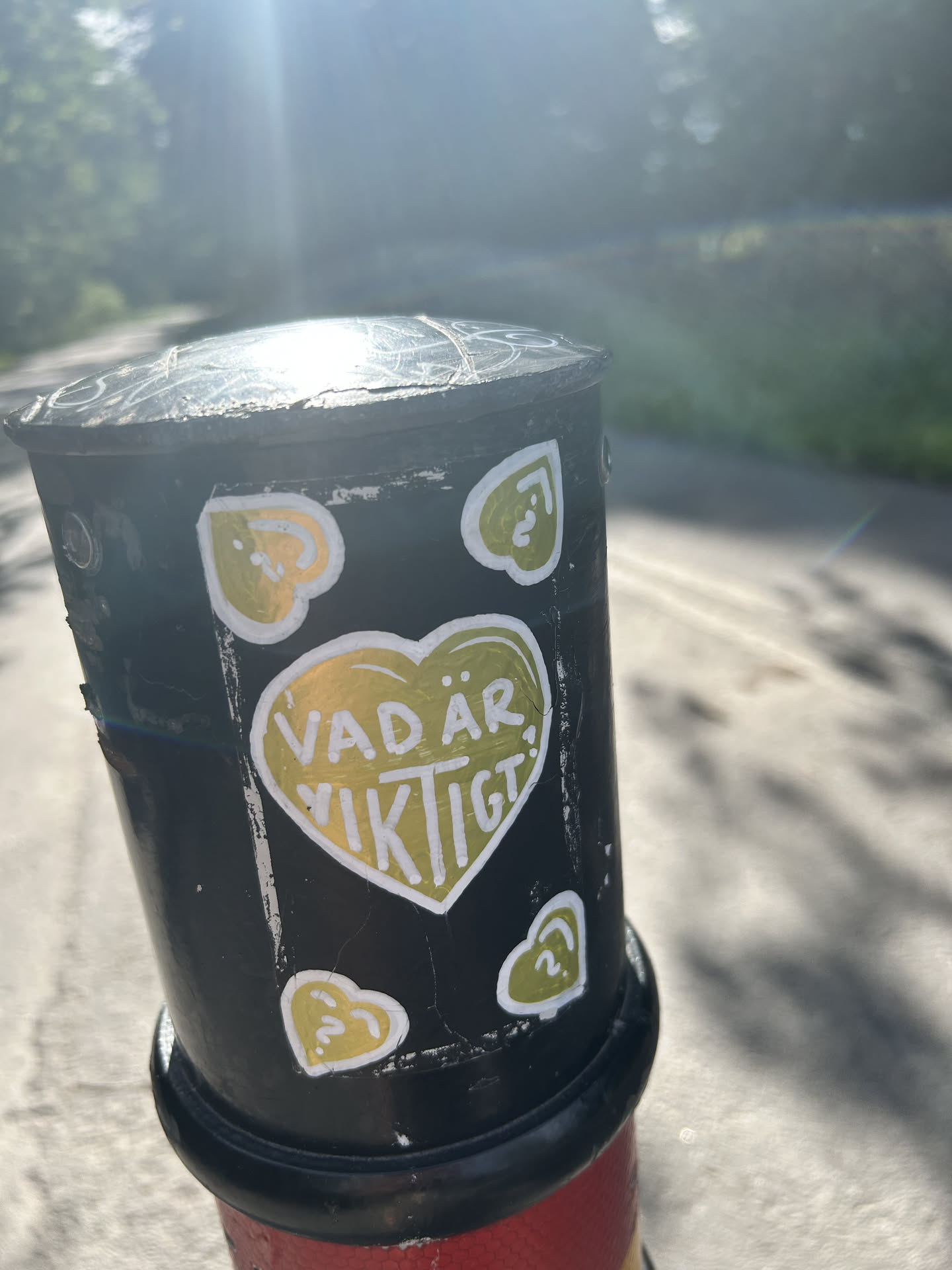 A black rectangular sticker on a post featuring a large central olive-green heart with the white text 'VAD ÄR VIKTIGT?'. Four smaller hearts containing question marks are located in the corners.