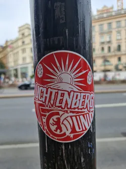 Street sticker Red and white circular sticker featuring a stylized sun, mountains, and the text "Lichtenberg Union."  A bear graphic is prominently displayed at the bottom. The sticker appears to be promoting a group or organization.