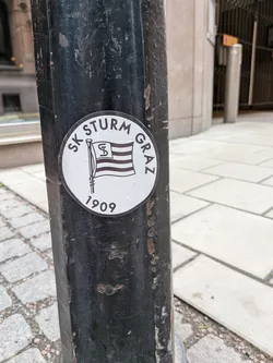 Street sticker A circular black and white sticker featuring the SK Sturm Graz logo, depicting a striped flag with an 'S' emblem, the club name, and the founding year 1909.