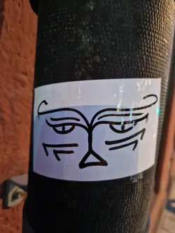 A simple yet captivating black and white drawing of a face on a sticker. The style is minimalist with bold lines and a focus on the eyes.