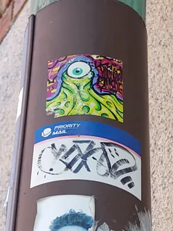 Street sticker A vibrant sticker featuring a psychedelic, one-eyed creature with tentacles. The creature is predominantly green and yellow, set against a background of multicolored graffiti-style elements.  The style is reminiscent of 1990s cartoons or underground comix.