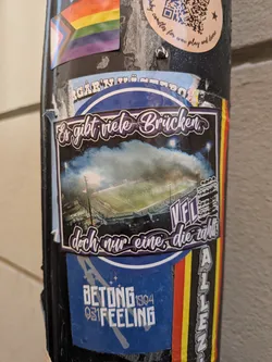 A rectangular sticker depicting an aerial view of a football stadium illuminated at night with smoke. It features stylized purple German text at the top and bottom, and 'VfL' on the right side.
