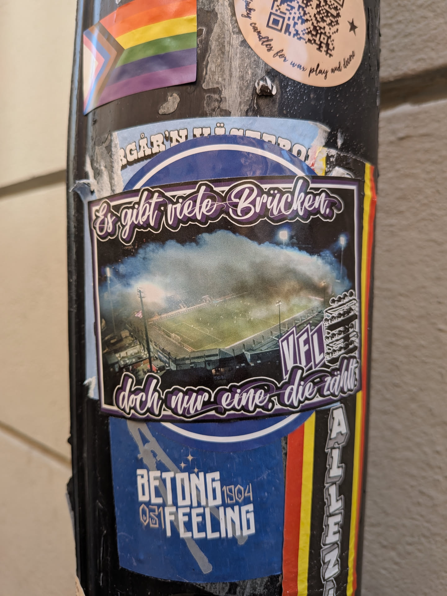 A rectangular sticker depicting an aerial view of a football stadium illuminated at night with smoke. It features stylized purple German text at the top and bottom, and 'VfL' on the right side.