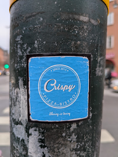 Street sticker A light blue square sticker with the logo of Crispy Pizza Bistro. The logo is a round emblem with the text "Crispy" in a stylized font, and underneath it says "Pizza Bistro." At the top of the emblem, it says "Since 2015." At the bottom of the sticker, it says "Sharing is caring."