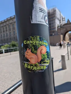 Street sticker An oval sticker depicting a red squirrel holding a nut in a park setting. It features green Cyrillic text outlined in black at the top and bottom.