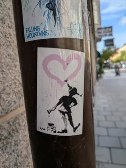 Street sticker A rectangular white sticker featuring a black silhouette of a girl with braided pigtails holding a paintbrush. Above her is a large, dripping pink heart. A paint can sits at her feet, and the text 'IRON' is printed in the bottom-left corner.