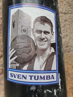 Street sticker A grayscale sticker featuring Sven Tumba, a famous Swedish ice hockey player, holding a soccer ball with a building in the background.  The sticker has a blue border and "SVEN TUMBA" is written at the bottom.