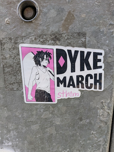 A sticker that says "Dyke March" with an illustration of a person with dreadlocks.