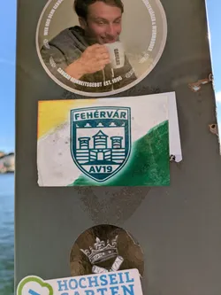 Street sticker This is a sticker for the Hungarian ice hockey team, Fehérvár AV19. The sticker features a stylized version of the team's crest. The background is a gradient of yellow, white, and green. The crest is green and white and features a stylized building and the text 'FEHÉRVÁR' and 'AV19'.