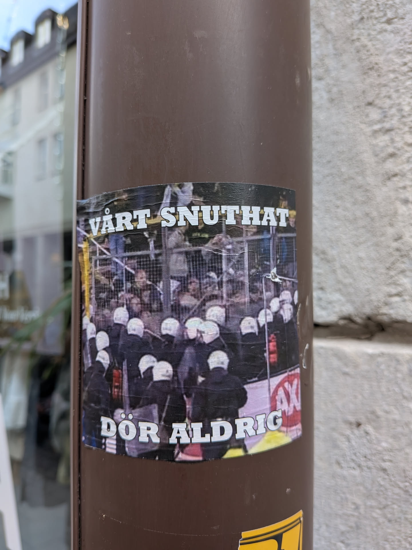 A rectangular sticker depicting a crowd of riot police wearing white helmets and dark uniforms, viewed from behind near a metal fence. Bold white text with black outlines is positioned at the top and bottom.