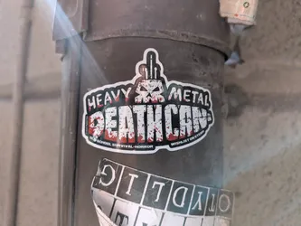 Street sticker A die-cut sticker featuring a stylized skull with a middle-finger gesture on top. The main text reads 'HEAVY METAL DEATH CAN' in a distressed, blood-splattered font. Subtext promotes it as an 'old-school survival-horror' game to wishlist on Steam.