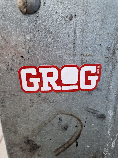 Street sticker Red and white sticker with the word Grog on it. The sticker has a slightly worn appearance and is placed on a grey metallic surface.