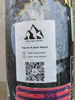 Street sticker A sticker featuring a mountain range logo and a call to action to tag the account in stories.  It includes Instagram and YouTube usernames and a QR code.
