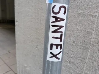 Street sticker A vertical white sticker with rounded corners adhered to a metal pole. It features the hand-written word 'SANTEX' in bold black marker.