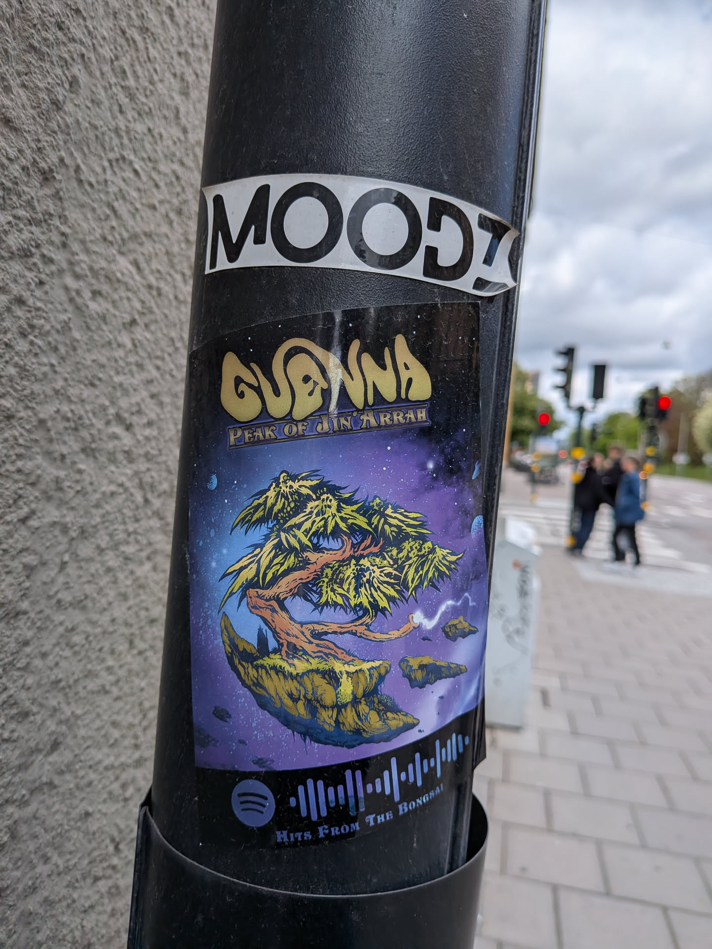 A vibrant, vertically oriented sticker featuring a fantastical cosmic landscape. The central image depicts a gnarled, ancient-looking tree with bright yellow-green foliage, rooted on a large, rugged floating island of rock and earth. Smaller rock fragments drift around it. The background is a deep purple and blue starry nebula, suggesting a vast outer space or mystical dimension. Above the tree, the artist's name 'GUENNA' is written in a bold, golden, stylized font. Below it, 'PEAK OF JIN ARRAH' appears in a smaller, more intricate script. At the bottom, a light blue Spotify logo is accompanied by a graphic representation of a sound wave, with the text 'HITS FROM THE BONGSAI' underneath.