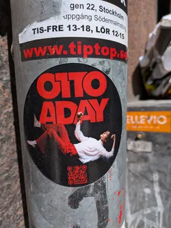 Street sticker The central sticker is circular with a matte black background. At the top, the name "OTTO ADAY" is prominently displayed in large, bold, red sans-serif capital letters. Below the text, a person is depicted lying on their back, looking upwards, with their arms slightly raised. The person is wearing loose-fitting red pants and a light-colored (likely white or cream) long-sleeved shirt, with bare feet visible. In the bottom right quadrant of the black circle, there is a small, red QR code. The overall design is modern and eye-catching, using a strong contrast between red and black.