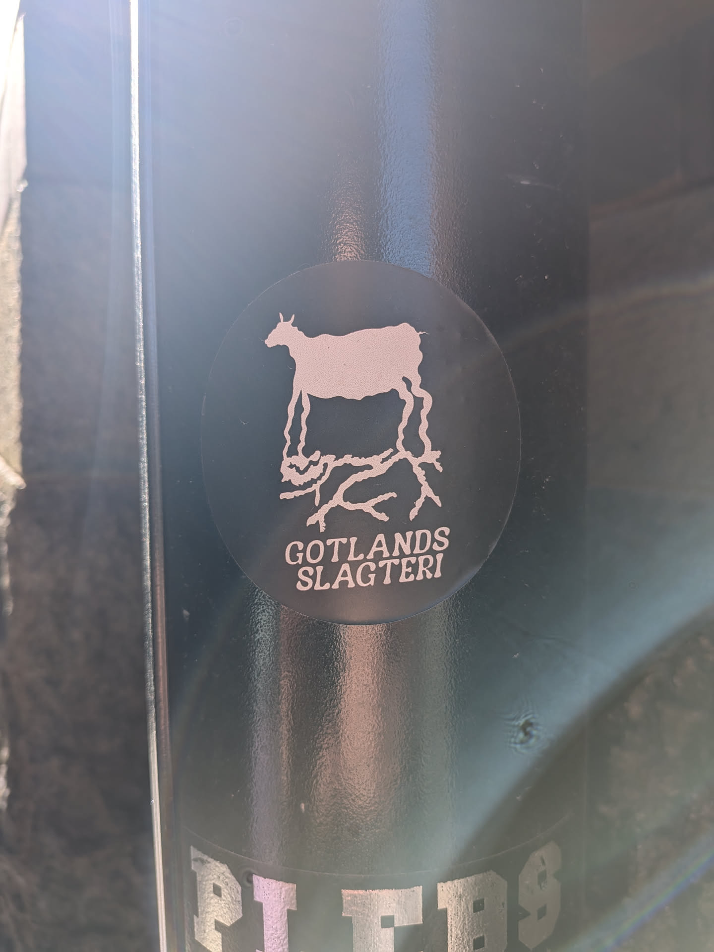 The sticker is circular with a dark, likely black or very dark grey, background. Centered on the sticker is a light-colored, almost white or pale pink, silhouette of a goat-like animal. Its most distinctive feature is that its legs are depicted as intricate, branching root-like structures that extend downwards. Below the animal and its roots, in the same light color, is the text "GOTLANDS SLAGTERI" arranged in two lines. The overall design is minimalist and graphic.