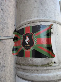 Street sticker Waving flag-shaped sticker with a red, green, and black Union Jack pattern. Centered is a black shield crest containing a white rooster, flanked by green laurel wreaths, with 'GLENTORAN ULTRAS' text.