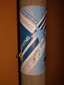 A blue and white sticker with a star design. Text on the sticker reads "Styrka", "Attityd", and what looks like "Djur". There are four stars at the top and a larger star incorporated into the design.  The sticker shows some signs of wear.