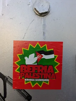 Street sticker A red sticker with a green starburst, a white dove, and a black and white flag. The text on the sticker says "Befria Palestina" and "Krossa sionismen".