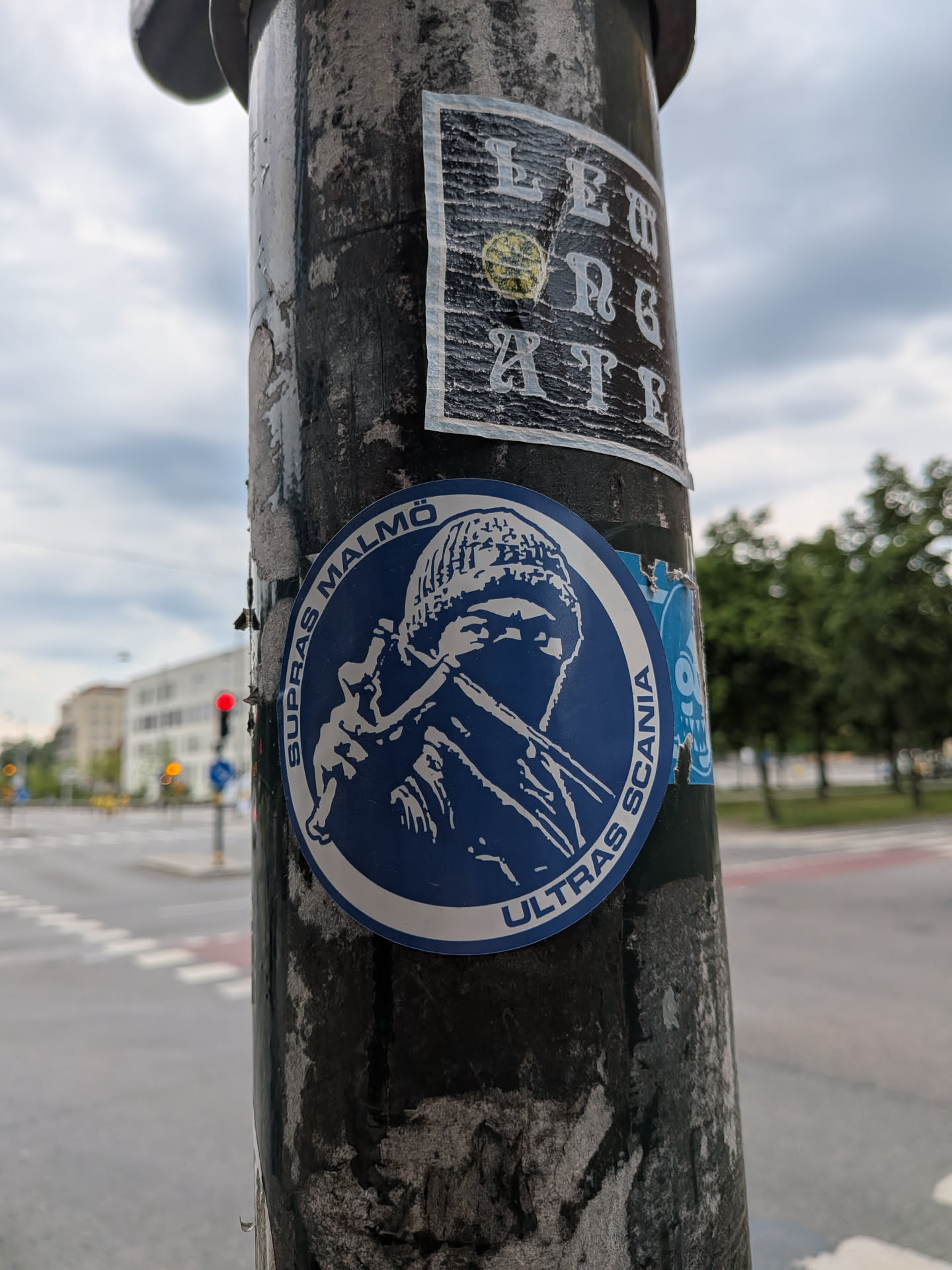 A circular blue sticker featuring a white stencil-style graphic of a masked figure in a beanie. The text 'SUPRAS MALMÖ' and 'ULTRAS SCANIA' curves along the border.