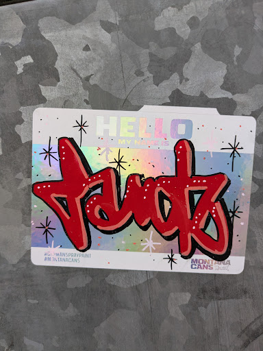 Street sticker This sticker showcases a graffiti-style red tag with a black outline on a holographic 'Hello My Name Is' sticker. The text on the sticker says 'Hello, My Name Is'. The tag appears to read 'Tantz'. The sticker has social media references to #GLYMANSPRAYPRINT and #MONTANACANS.