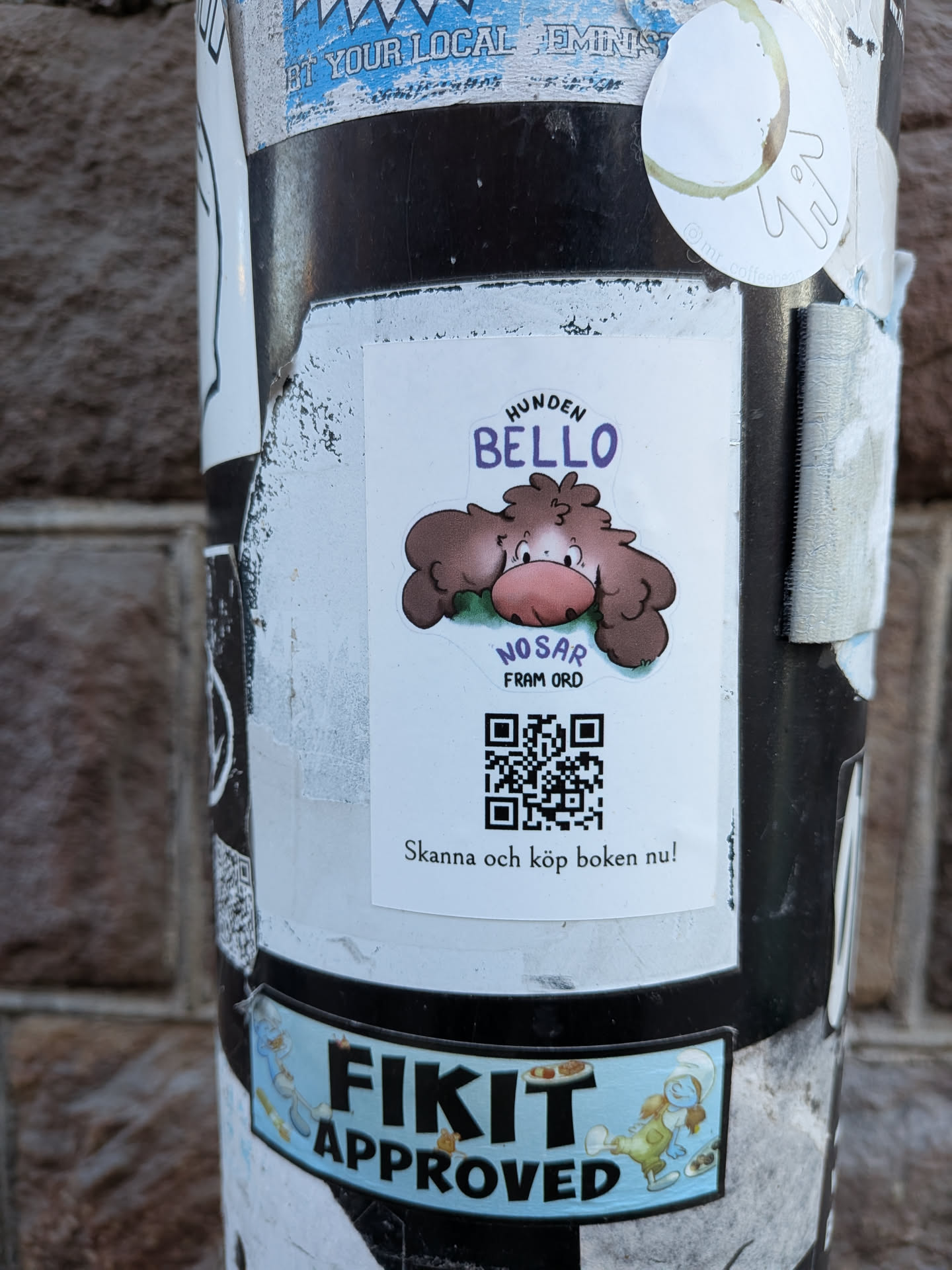 A rectangular sticker with slightly rounded corners, featuring a charming cartoon illustration of a fluffy brown dog named Bello. Bello has large, floppy ears, a prominent pink snout, and small, dark eyes, appearing to be resting on a patch of green. Above the dog, the text "HUNDEN BELLO" is written in purple, with "HUNDEN" in a smaller font and "BELLO" in a larger, playful script. Below the dog, in purple, is "NOSAR FRAM ORD" (Sniffs out words). The bottom half of the sticker contains a black and white QR code, beneath which is the call to action "Skanna och köp boken nu!" (Scan and buy the book now!) in black text. The background of the sticker is white.