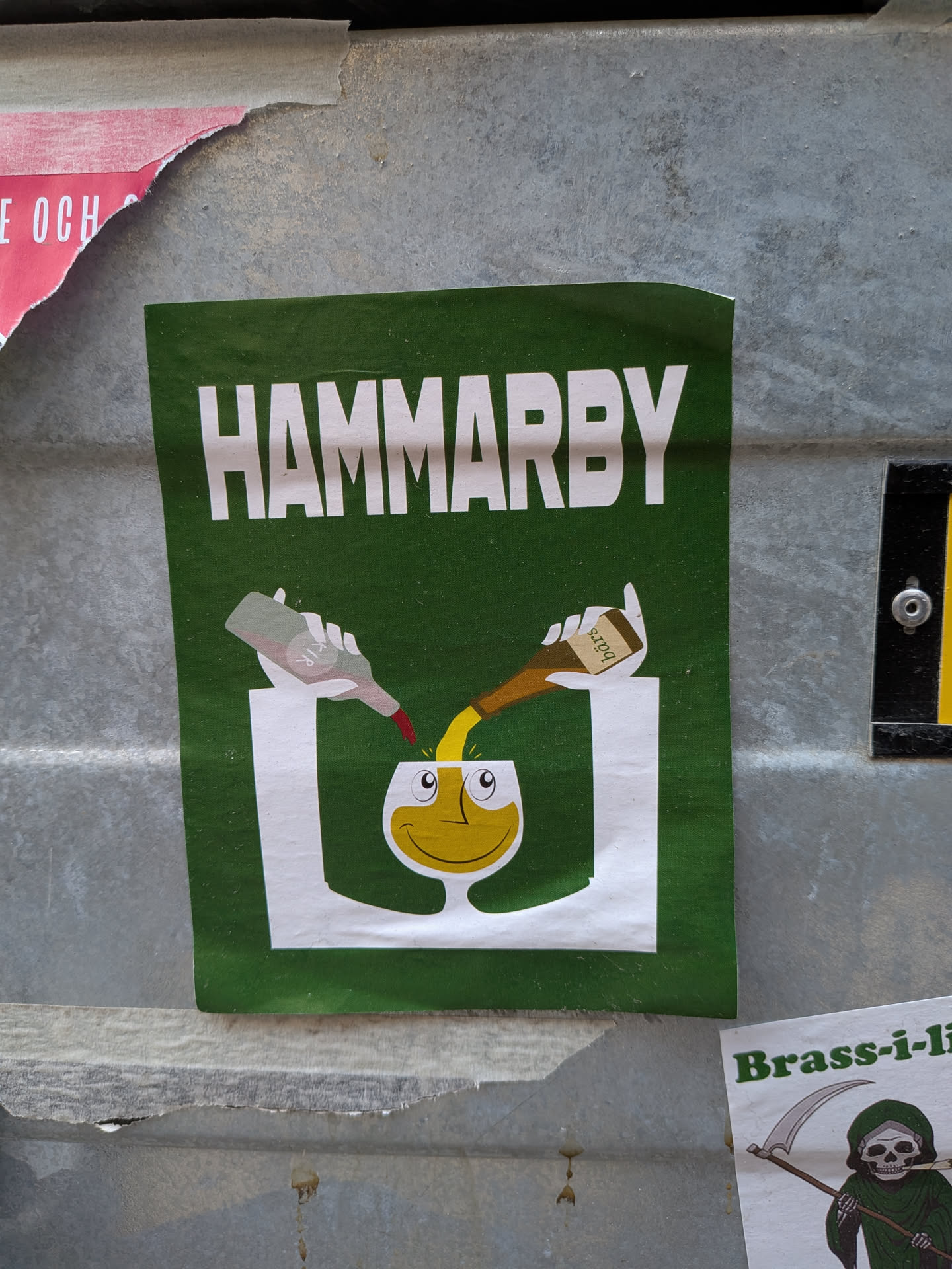 A rectangular sticker with a dark green background. At the top, the word 'HAMMARBY' is written in large, bold white capital letters. Below the text, a cartoon illustration depicts two stylized white hands. The left hand holds a light grey bottle with a red cap, labeled 'KIR', pouring a red liquid. The right hand holds a brown bottle with a white label, labeled 'Bärs', pouring a yellow liquid. Both liquids are being poured into a white, stylized glass that features a yellow, smiling face with two white eyes and black pupils looking upwards. The overall design is simple and graphic, using the club's green and white colors.