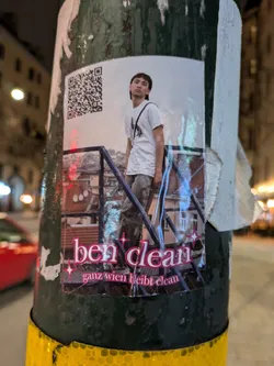 Street sticker A sticker featuring a photo of a person standing on a staircase, with the text 'ben clean' and 'ganz wien bleibt clean' written underneath.  A QR code is also present on the sticker.