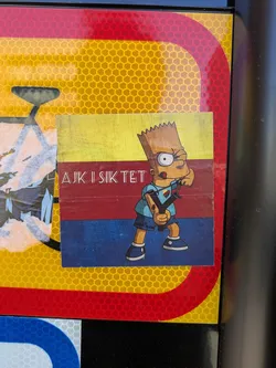 Street sticker A square sticker featuring Bart Simpson holding a slingshot, with a yellow and red background. The text on the sticker reads 'AJK I SIK TET'.