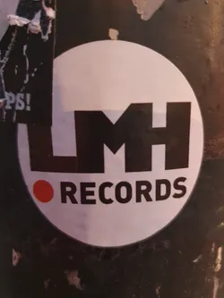 A round white sticker with the text LMH RECORDS in black bold letters. A small red dot precedes the word RECORDS. The sticker is affixed to a dark-colored surface.