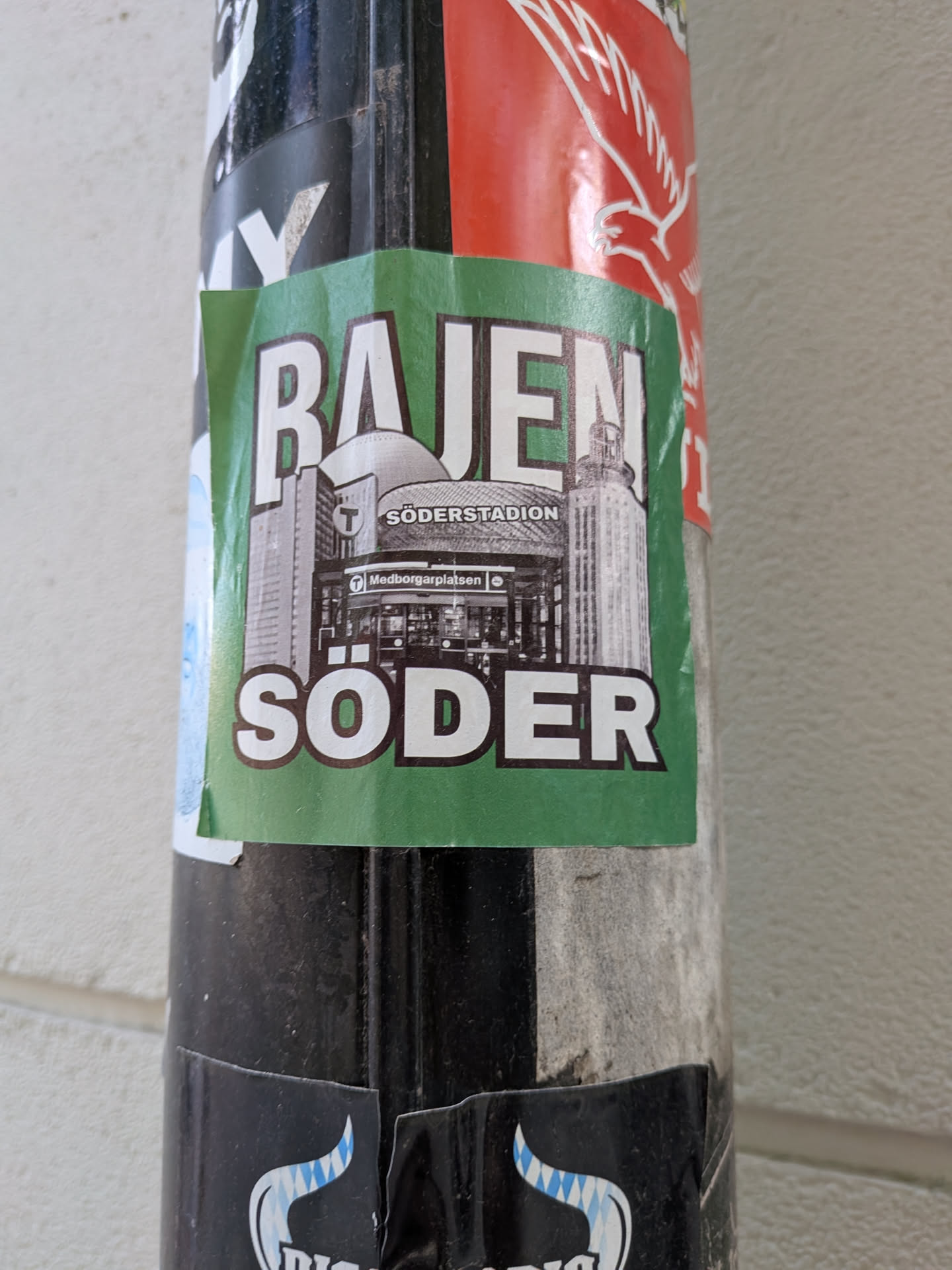 A square green sticker depicting Södermalm landmarks in black and white, including Söderstadion and Medborgarplatsen. Bold white text reads 'BAJEN' at the top and 'SÖDER' at the bottom.