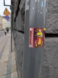 Street sticker The sticker is rectangular with a red border. The main illustration depicts a stylized figure with a sun-like head radiating yellow rays. The figure has a yellow torso and red pants, and is holding a lute-like instrument. The background is a dark, reddish-brown. To the left of the illustration, vertically oriented text reads 'konst.se/listigspindel Mikael Jonsson' in white. Below this text is a QR code. A small yellow section with text is visible to the right of the main illustration.