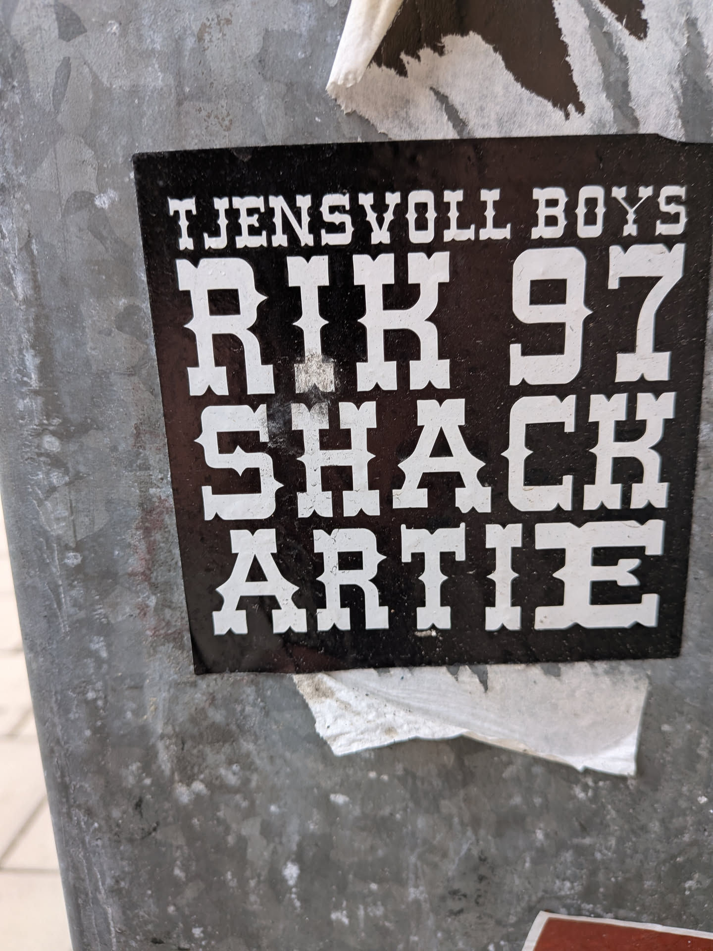 A square black sticker featuring white text in a bold, Western-style serif font. The text is stacked in four lines on a solid black background, reading 'TJENSVOLL BOYS', 'RIK 97', 'SHACK', and 'ARTIE'.