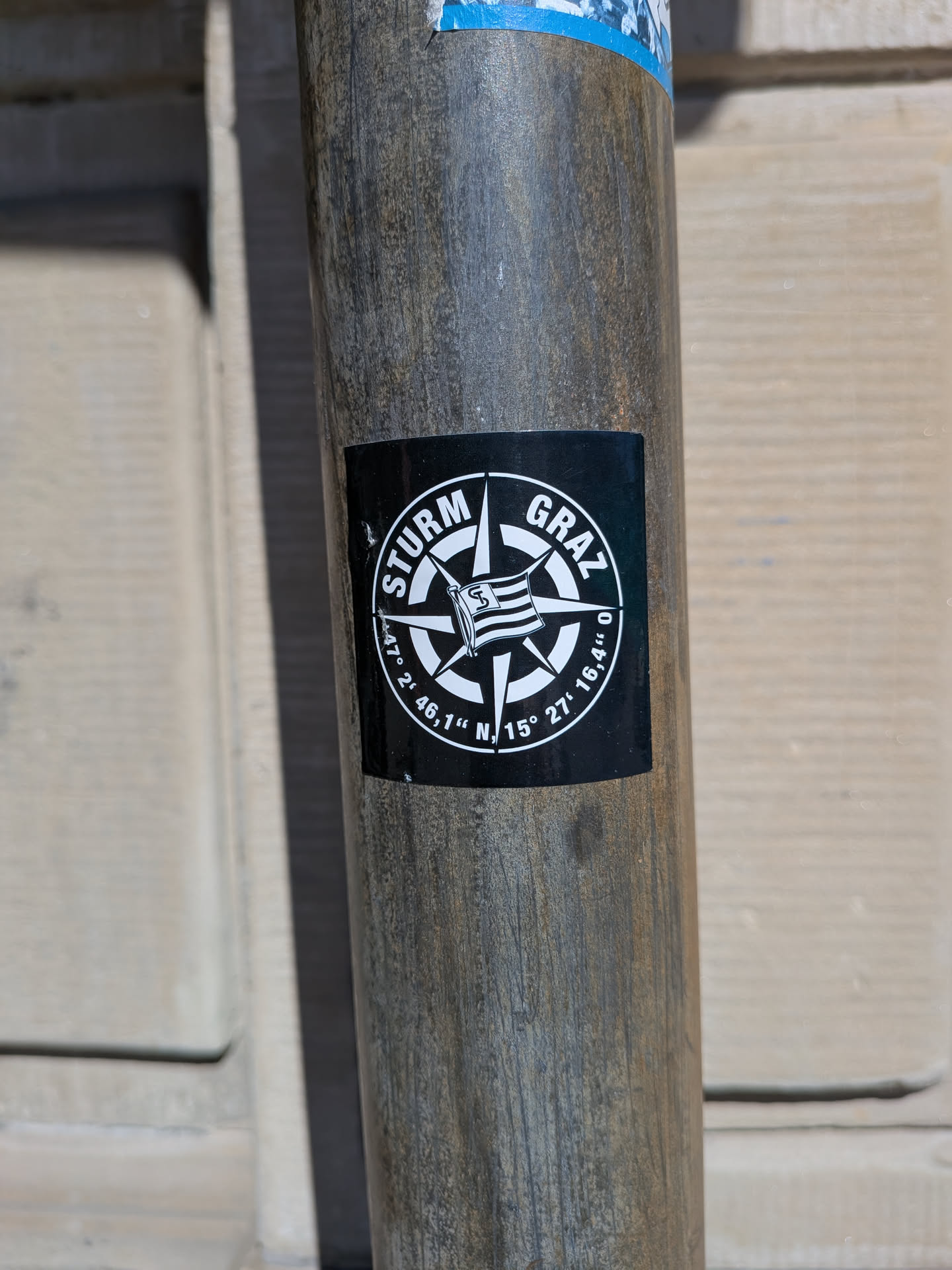 A square, black and white sticker featuring a prominent compass rose design. In the center of the compass, a stylized flag with horizontal stripes and a letter 'S' is depicted. The top arc of the circular border around the compass reads 'STURM GRAZ' in white capital letters. The bottom arc displays geographical coordinates: '47° 2' 46,1'' N, 15° 27' 16,4'' O'. The sticker has a clean, graphic style.